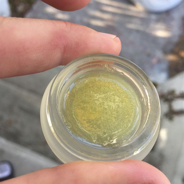 Jar of bright yellow live rosin held in daylight